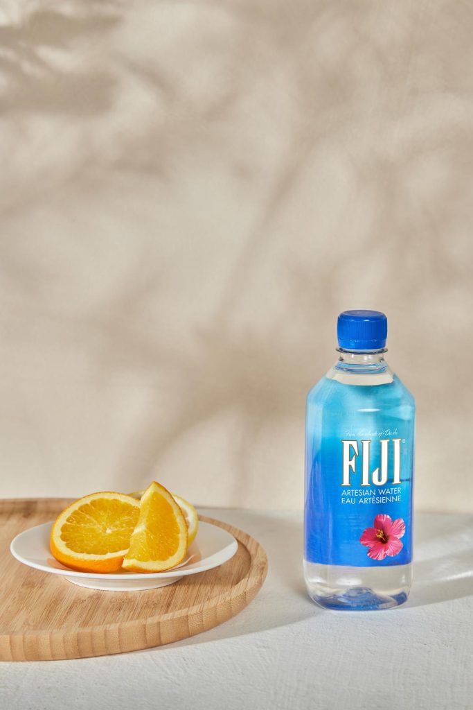 Product Photography - Bottle of Fiji water on a table, next to plate of oranges - Mount Studio