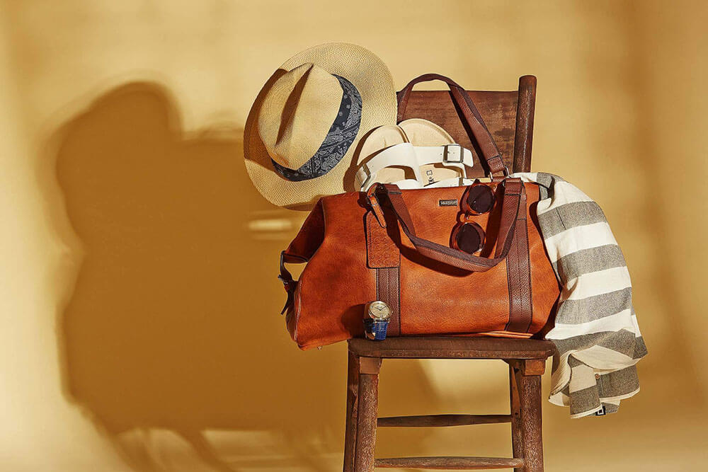 Freelance Product photography - brown leather duffle bag on wooden chair with hat, shirt and sandals - Mount Studio